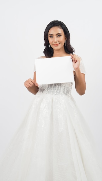 Belle femme asiatique sexy TAN SKIN en robe de mariée tenir du papier blanc vierge ou vide sur fond blanc.