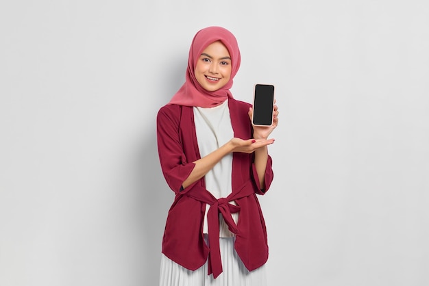 Belle femme asiatique souriante en chemise décontractée montrant un écran vide de téléphone portable et regardant la caméra isolée sur fond blanc