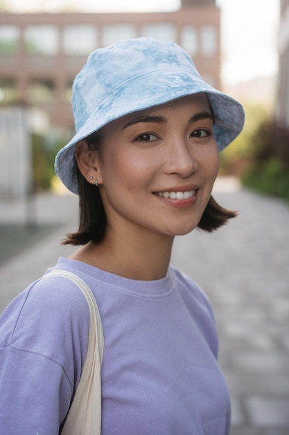 Belle femme asiatique souriante portant des vêtements décontractés, panama élégant regardant la caméra à l'extérieur