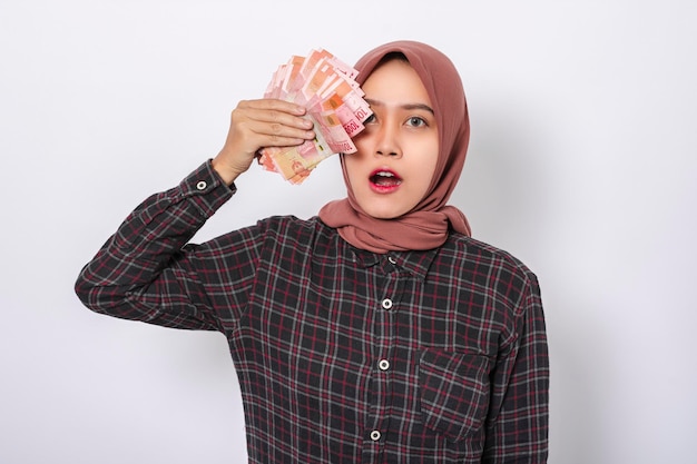 Belle femme asiatique souriante tenant de l'argent en roupie indonésienne debout sur fond blanc isolé