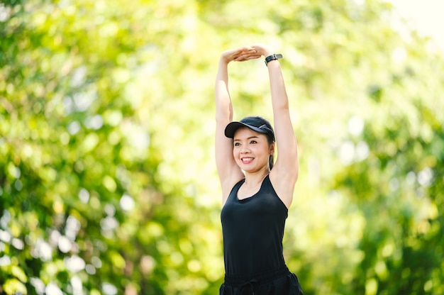 Belle femme asiatique de sport d'âge moyen étirant ses bras et regardant loin avant la séance d'entraînement physique au parc