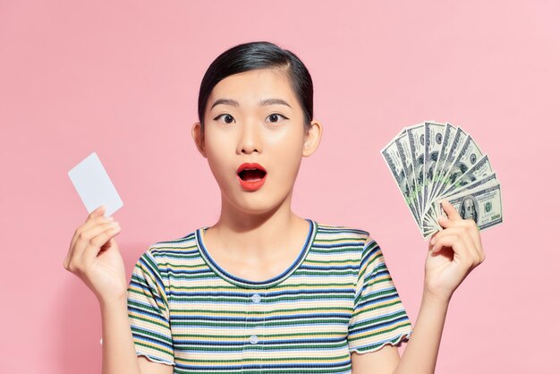 Photo belle femme asiatique tenant de l'argent et des cartes isolées sur un fond rose