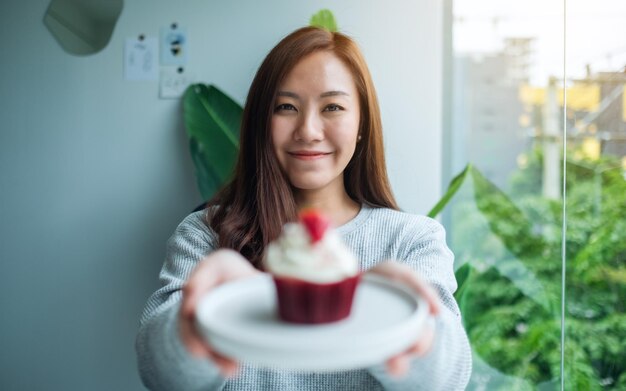 Une belle femme asiatique tenant une assiette de cupcake de velours rouge