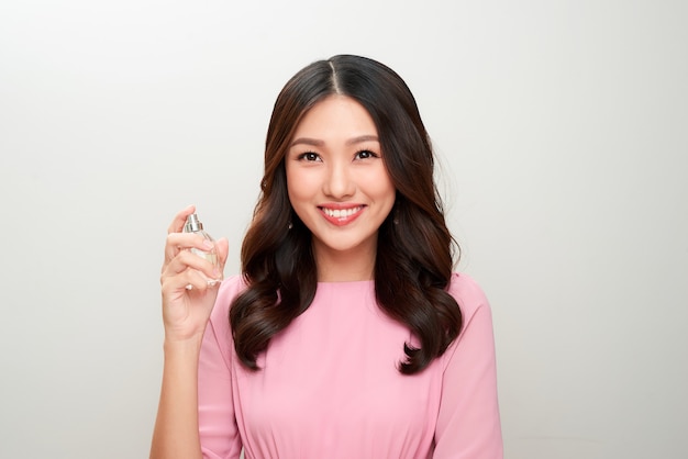 Belle femme asiatique tenant une bouteille de parfum et l'appliquant