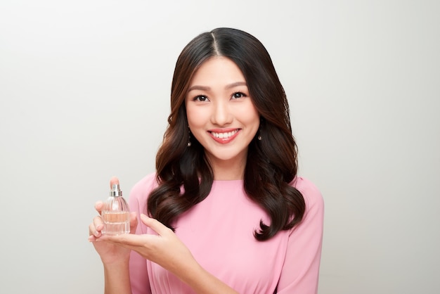 Belle femme asiatique tenant une bouteille de parfum et l'appliquant