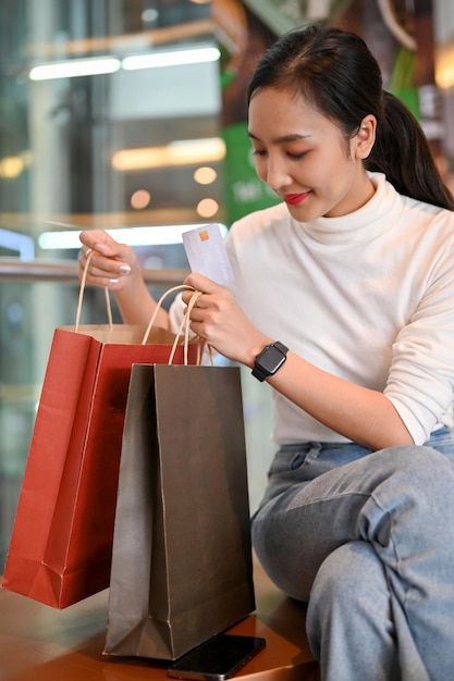 Belle femme asiatique tenant une carte de crédit ouvrant ses sacs tout en se reposant dans le centre commercial