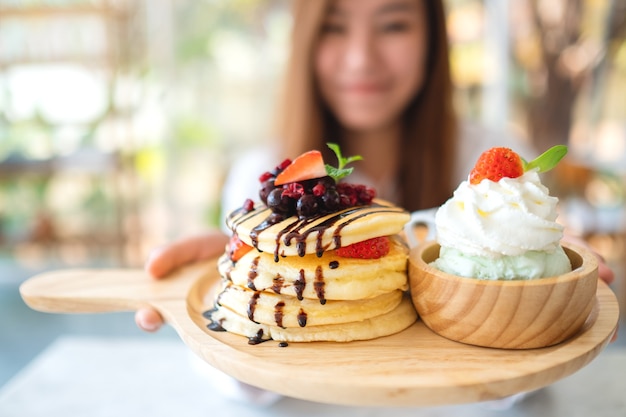 Une belle femme asiatique tenant et montrant une assiette de crêpes avec de la crème glacée et de la crème fouettée au café