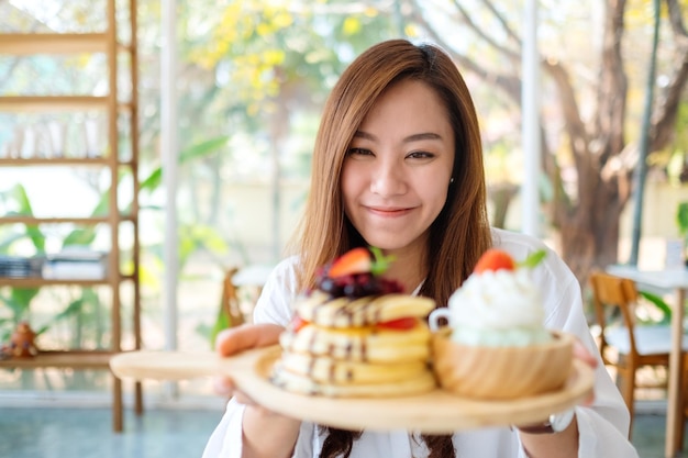 Une belle femme asiatique tenant et montrant une assiette de crêpes avec de la crème glacée et de la crème fouettée au café