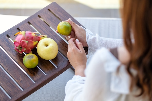 Une belle femme asiatique tenant une orange avec poire et fruit du dragon sur une petite table en bois