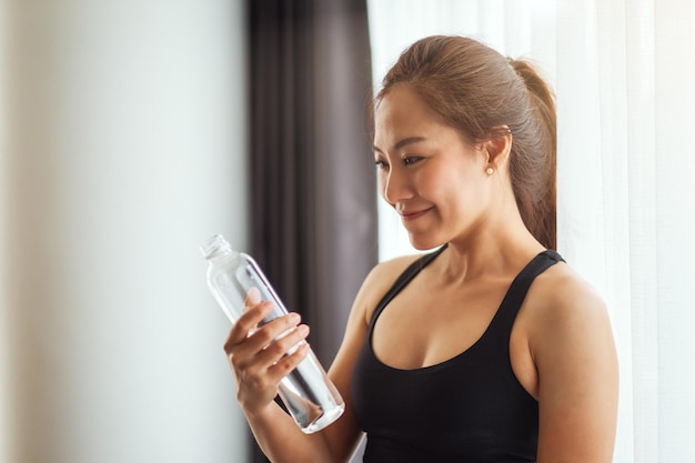 Une belle femme asiatique tenant et regardant une bouteille d'eau tout en faisant de l'exercice