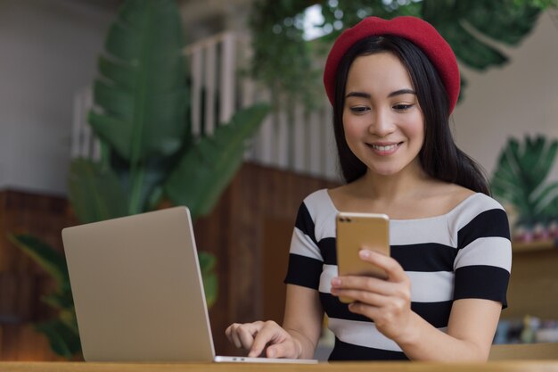 Belle femme asiatique tenant un smartphone, communication, streaming vidéo en ligne. Pigiste utilisant un ordinateur portable, travaillant à domicile