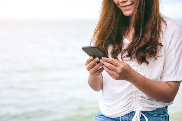 Une belle femme asiatique tenant et utilisant un téléphone portable au bord de la mer