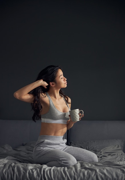 Belle femme asiatique tient une tasse de café et apprécie le soleil du matin