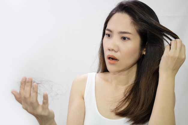 Une belle femme asiatique touche ses cheveux et regarde la perte de cheveux sous la main avec un choc et incroyable