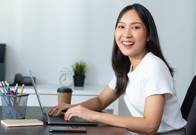 Belle femme asiatique utilisant un ordinateur portable et assise près de la table au bureau à domicile.