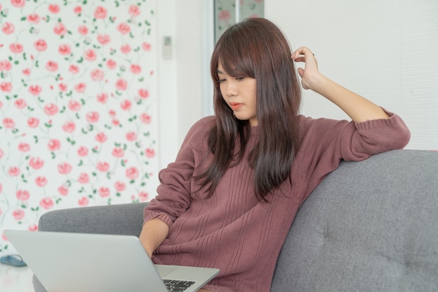 Belle femme asiatique utilisant un ordinateur portable sur un canapé dans le salon