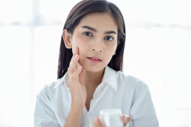 Une belle femme asiatique utilisant un produit de soin de la peau, une crème hydratante ou une lotion en prenant soin de son teint sec. Crème hydratante dans les mains féminines.