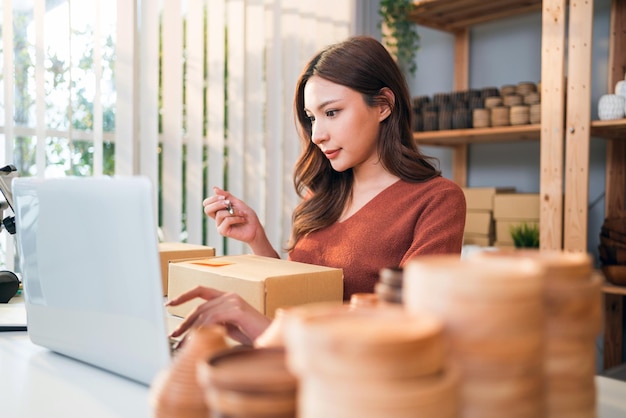 Une belle femme asiatique vend des produits de vase en ligne en direct à la maison Une jeune fille séduisante écrit l'adresse du client sur le colis à envoyer Concept d'achat et d'achat à distance