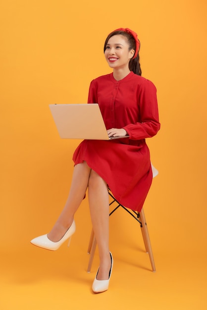 Belle femme asiatique vêtue d'une robe rouge et debout sur un fond orange