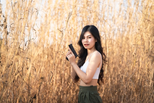 Belle femme asiatique vise le pistolet sur l'herbe sèche