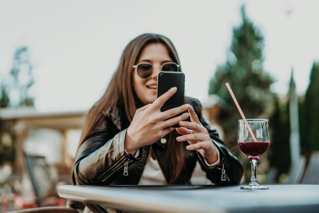 Belle femme assise dans un café, buvant un cocktail et utilisant un smartphone. Étudiant pendant la pause au café. Mode de vie, technologie