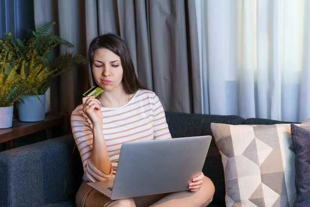 Belle femme assise dans le salon faisant du shopping en ligne avec paiement pratique par carte de crédit à l'aide de dig