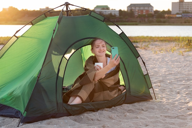 Belle femme assise dans la tente et prendre une photo. Camping près de l'eau. Vacances en plein air.