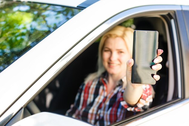 Photo belle femme assise dans une voiture et montrant son smartphone par la fenêtre