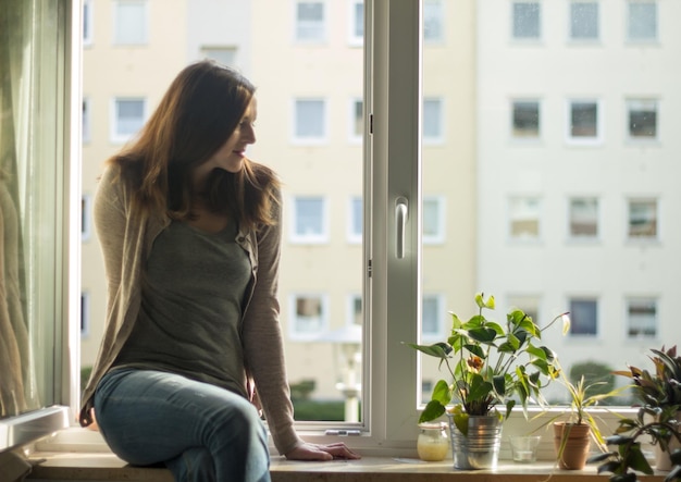 Photo une belle femme assise à la fenêtre à la maison.