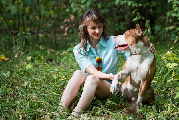 Belle femme assise sur l'herbe avec chien Pit-bull