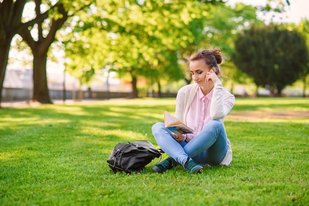 Belle femme assise sur l'herbe et livre de lecture dans le parc en été