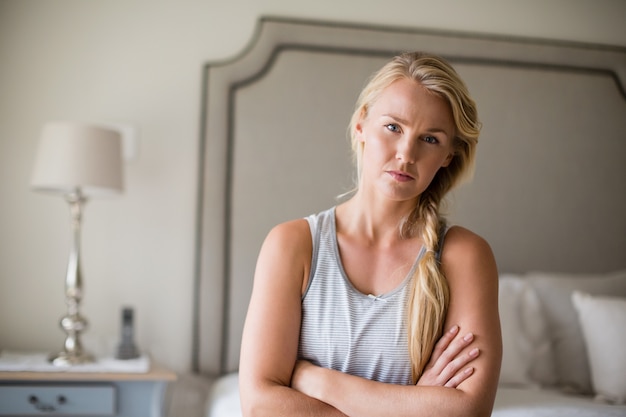 Belle femme assise sur le lit avec les bras croisés dans la chambre