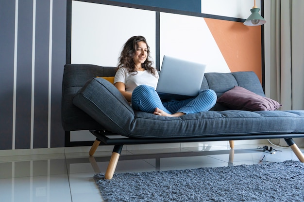 Belle femme assise avec un ordinateur portable sur un canapé dans une pièce élégante.