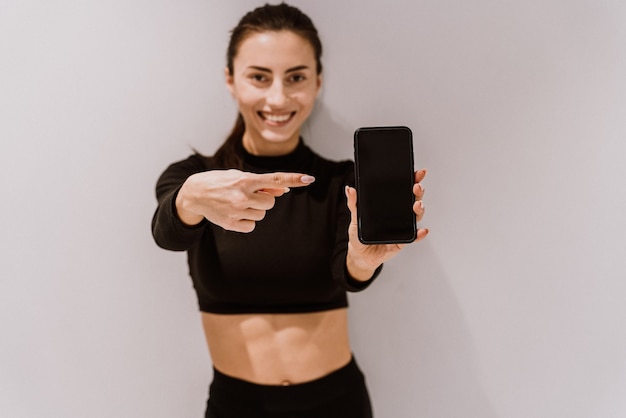 Belle femme athlétique affichant l'écran du téléphone mobile et pointant vers elle