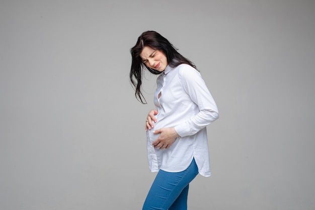 Belle femme attend un bébé, touche le ventre de femme enceinte ressentant une douleur sur fond gris studio. Début des douleurs de l'accouchement