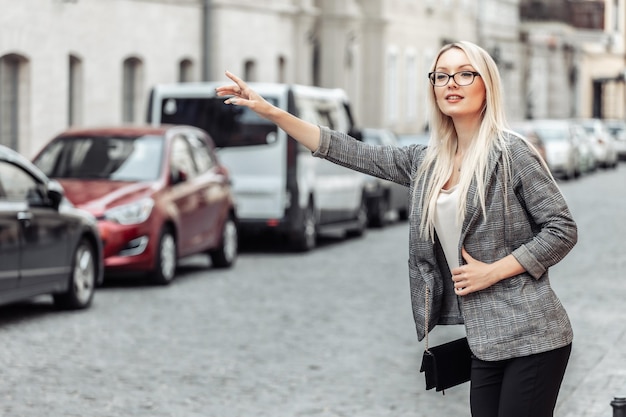 Belle Femme Attrapant Une Voiture De Taxi Dans La Rue. Portrait Femme d'affaires blonde sur le chemin du travail en arrêtant la voiture de taxi à l'extérieur.