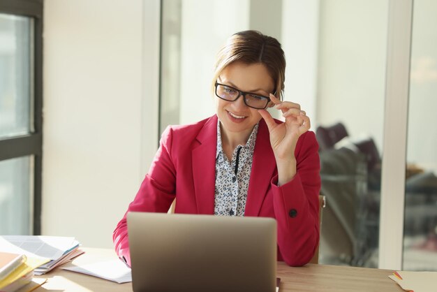 Une belle femme au bureau avant que l'ordinateur portable ne redresse les lunettes d'une entreprise en gros plan