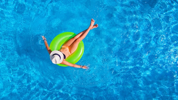 Belle femme au chapeau dans la piscine sur l'anneau gonflable dans l'eau en vacances