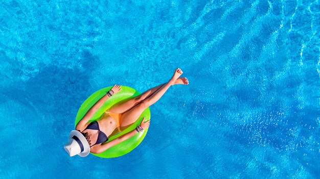 Belle femme au chapeau dans la piscine sur l'anneau gonflable dans l'eau en vacances