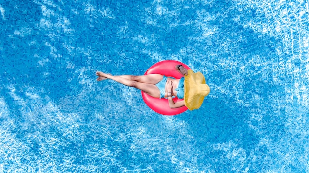 Belle femme au chapeau dans la piscine vue aérienne de dessus, jeune fille en bikini se détend et nage sur l'anneau gonflable et s'amuse dans l'eau en vacances en famille, tropical resort de vacances