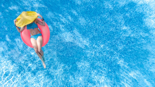 Belle femme au chapeau dans la piscine vue aérienne de dessus, jeune fille en bikini se détend et nage sur l'anneau gonflable et s'amuse dans l'eau en vacances en famille, tropical resort de vacances