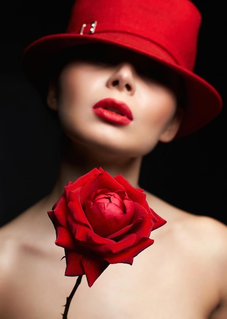 Belle femme au chapeau derrière une rose rouge