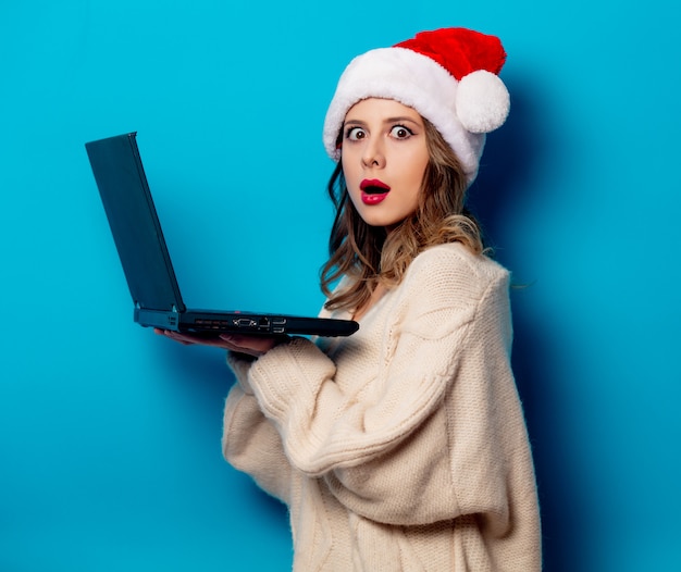 Belle femme au chapeau de Noël avec ordinateur portable sur le mur bleu