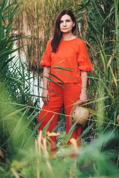 Belle femme au chapeau de paille vêtue de vêtements rouges sur fond de roseaux et de lac