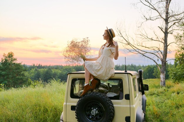 Belle femme au chapeau profitant du paysage à l'horizon assis à l'extérieur de la voiture