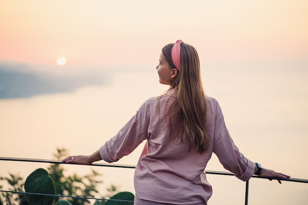 Une belle femme au coucher du soleil se dresse sur une terrasse surplombant la mer Photo de haute qualité