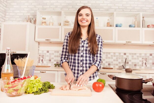 Belle femme au foyer souriante, cuisiner le dîner et couper la viande