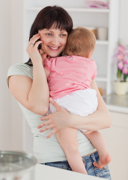 Belle femme au téléphone tout en tenant son bébé dans ses bras