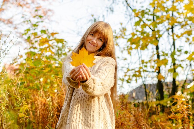 Belle femme d'automne debout près des feuilles d'automne colorées Joli modèle gai heureux regardant la caméra