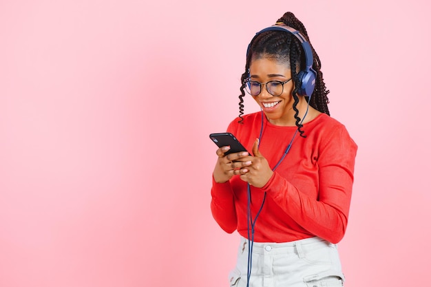 Belle femme aux cheveux afro écoutant de la musique et dansant sur fond rose